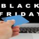 frase Black Friday na tela de um notebook, com uma mão na frente da tela, segurando um cartão de crédito, em busca de conversões