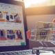 imagem de um computador aberto em um site de negócio virtual / e-commerce, com um carrinho de compras miniatura ao lado