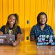 Dupla de jovens sentada com seus notebooks e sorrindo.