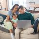 Um casal e uma criança sentados no sofá olhando para um notebook