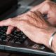 Mãos de pessoa idosa sobre o teclado de notebook