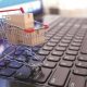 Imagem de uma miniatura de carrinho de supermercado sobre o teclado de um notebook