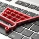 Imagem de um molde de carrinho de supermercado vermelho, em plano baixo, sobre o teclado de computador